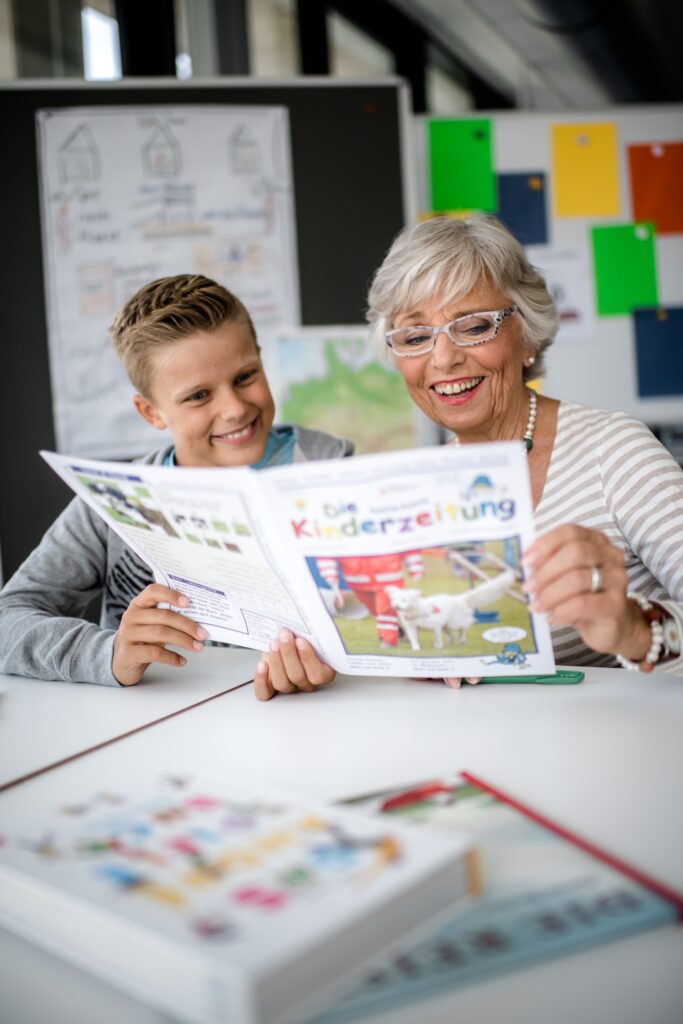 Foto von einemm Jungen und einer Frau, die an einem Tisch sitzen und gemeinsam in eine Kinderzeitung schauen